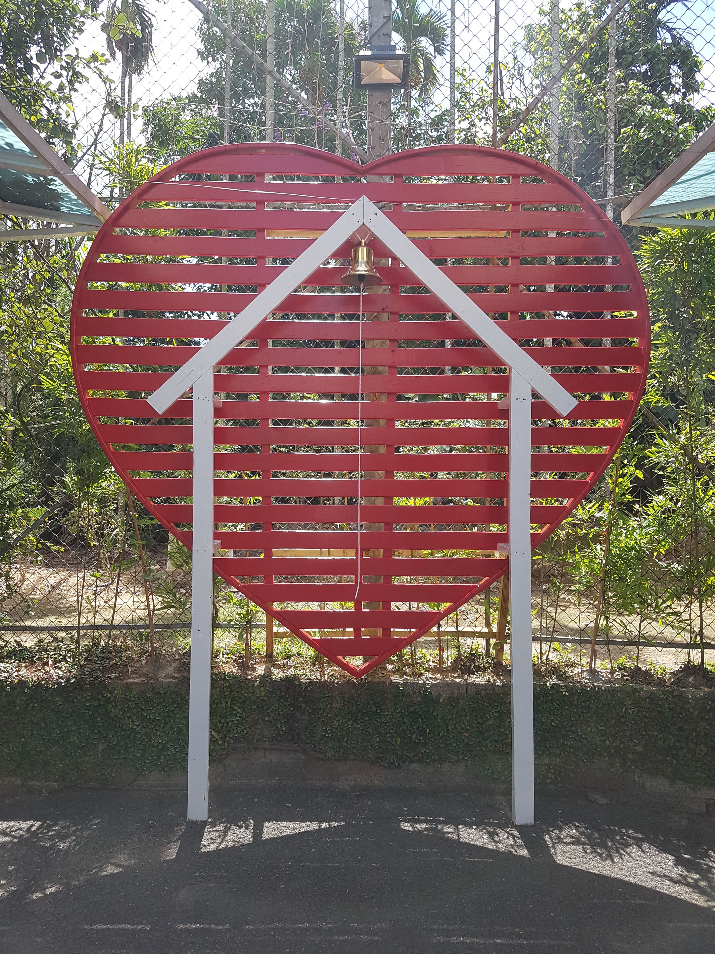 Una estructura con forma de corazón, marco blanco y una campana en la parte superior.