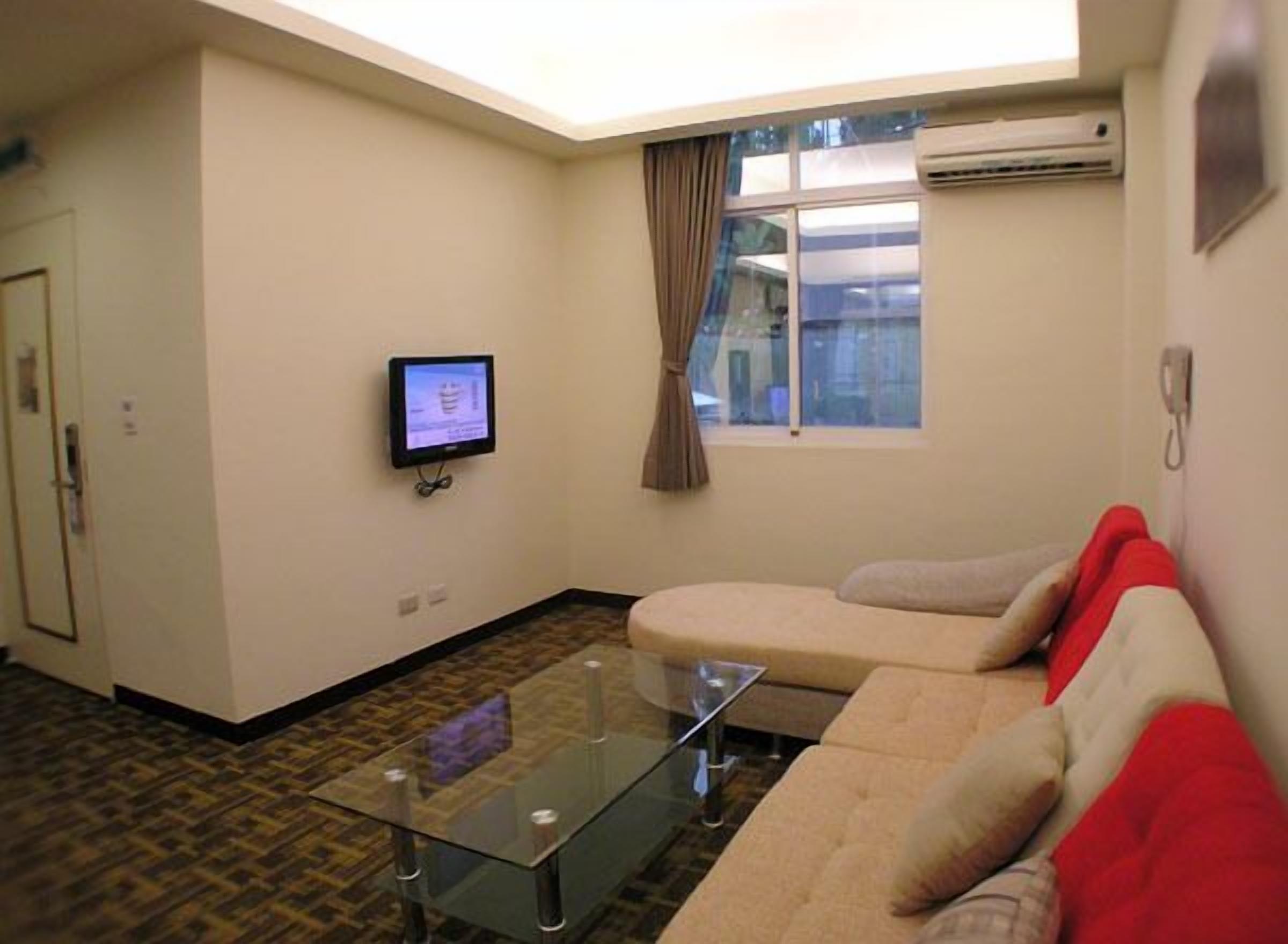 Una sala de estar con una mesa de centro de vidrio, un sofá color beige y un televisor de pantalla plana montado en la pared.
