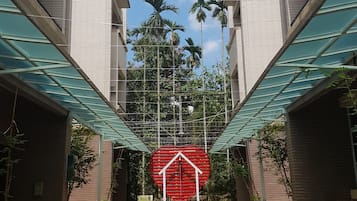 Entrada de un edificio con un letrero rojo en forma de casa, rodeada de palmeras y un cielo despejado.