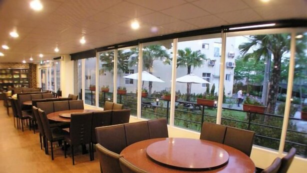 Un restaurant avec des tables et des chaises rondes, de grandes fenêtres offrant une vue sur les palmiers et les bâtiments.