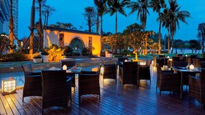 An outdoor dining area with wicker furniture and a small building with an archway.