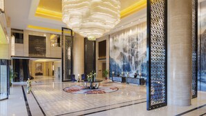 A spacious lobby with a large chandelier, a reception desk, and a decorative wall mural.