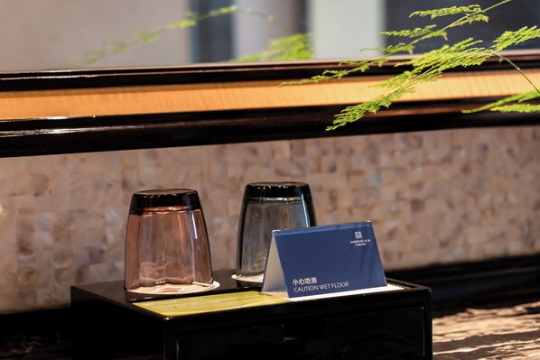 A caution wet floor sign on a black stand near a glass table with a plant in the background. - Wanda Realm Guangzhou Zengcheng (Guangzhou)