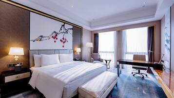 A hotel room with a large bed, a desk, and a chair. There is a painting on the wall and a window with curtains.