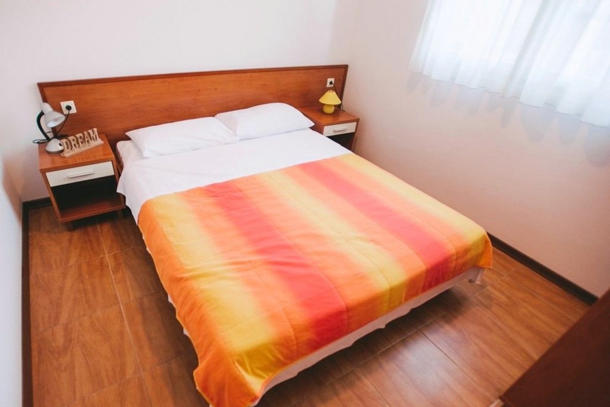 A neatly made bed with a gradient blanket, a wooden headboard, a bedside table with a lamp, and a nightstand with a lamp.