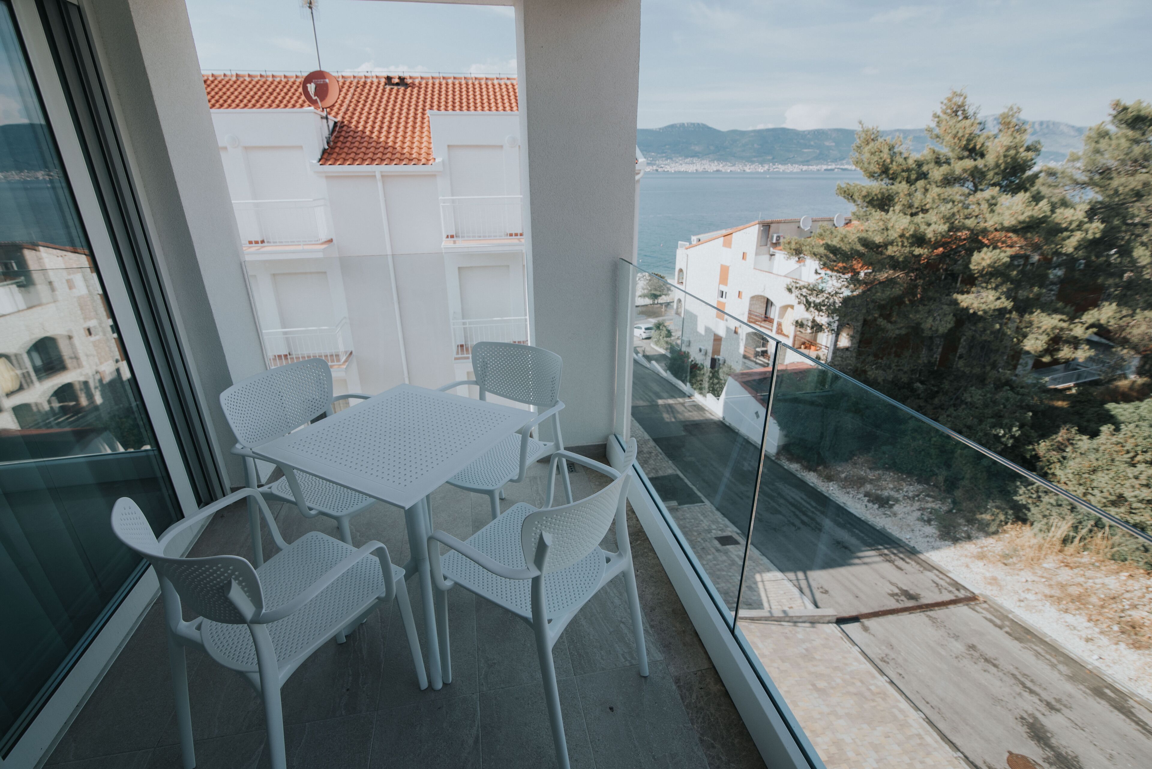 A balcony with a table and chairs, overlooking a coastal view with buildings and trees.