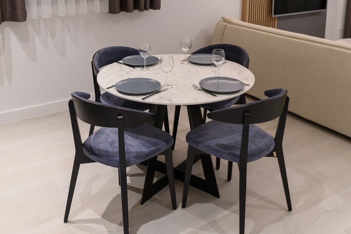 A dining area with a round table, four chairs, and a television in the background.