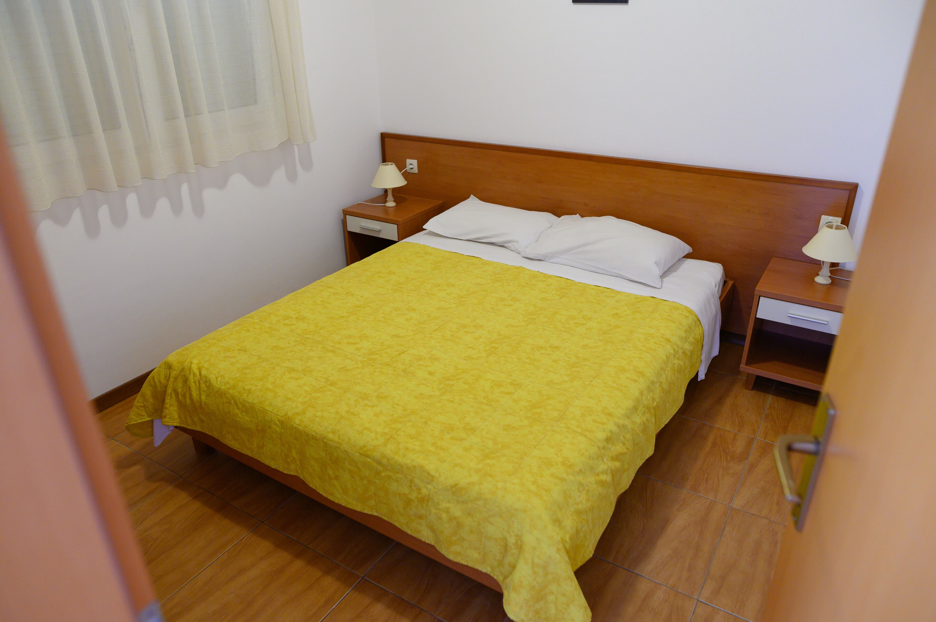 A single bed with a yellow bedspread in a room with wooden flooring and white walls.