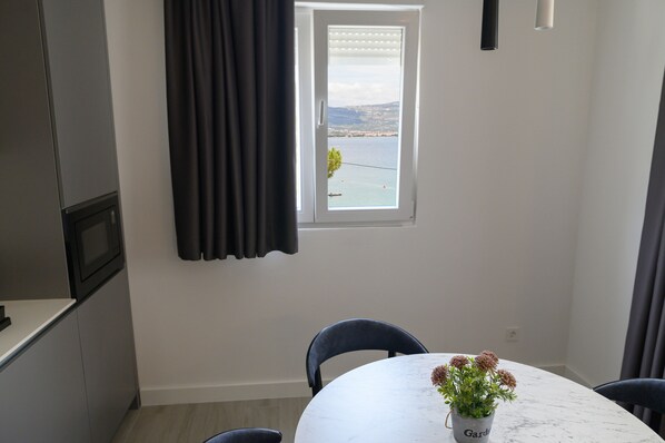 A dining area with a view of the sea through a window, a table with chairs, and a potted plant on the table. - Villa Malo More (Trogir)