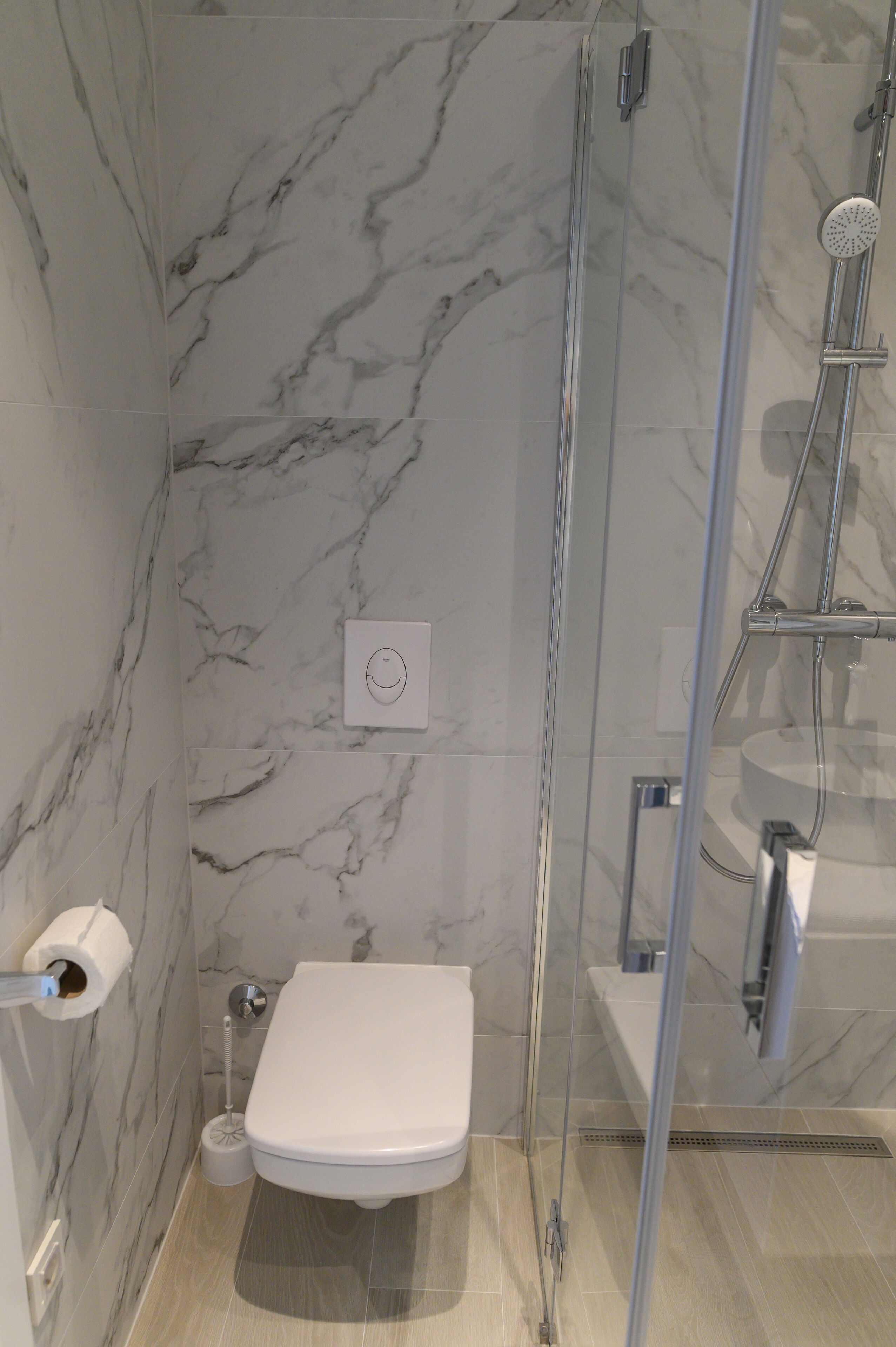 Un baño con pared de mármol, inodoro, cabina de ducha y dispensador de papel higiénico.