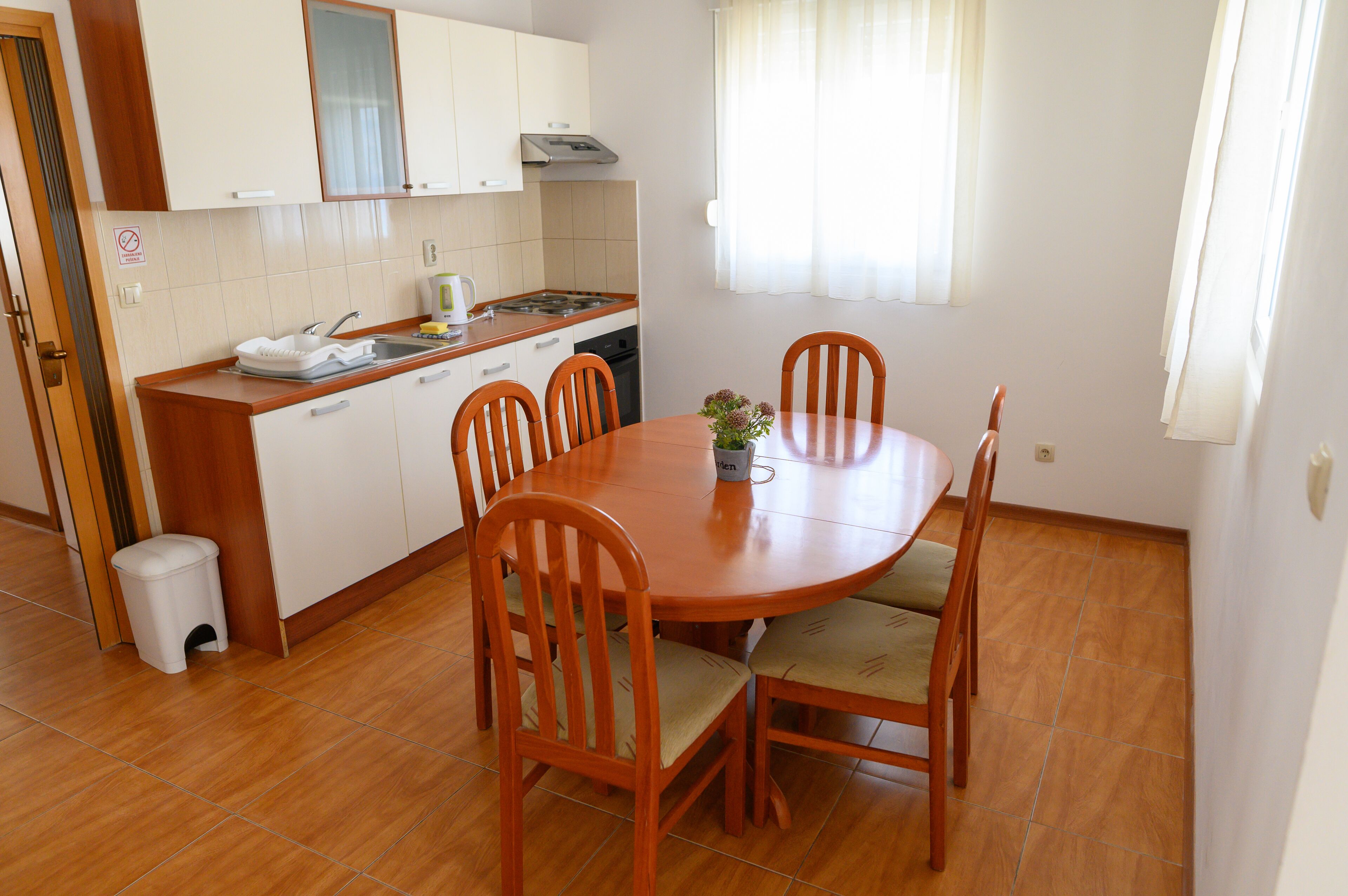Une cuisine compacte avec des meubles blancs, une cuisinière et un évier. On y trouve une table à manger avec quatre chaises et un vase rempli de fleurs.