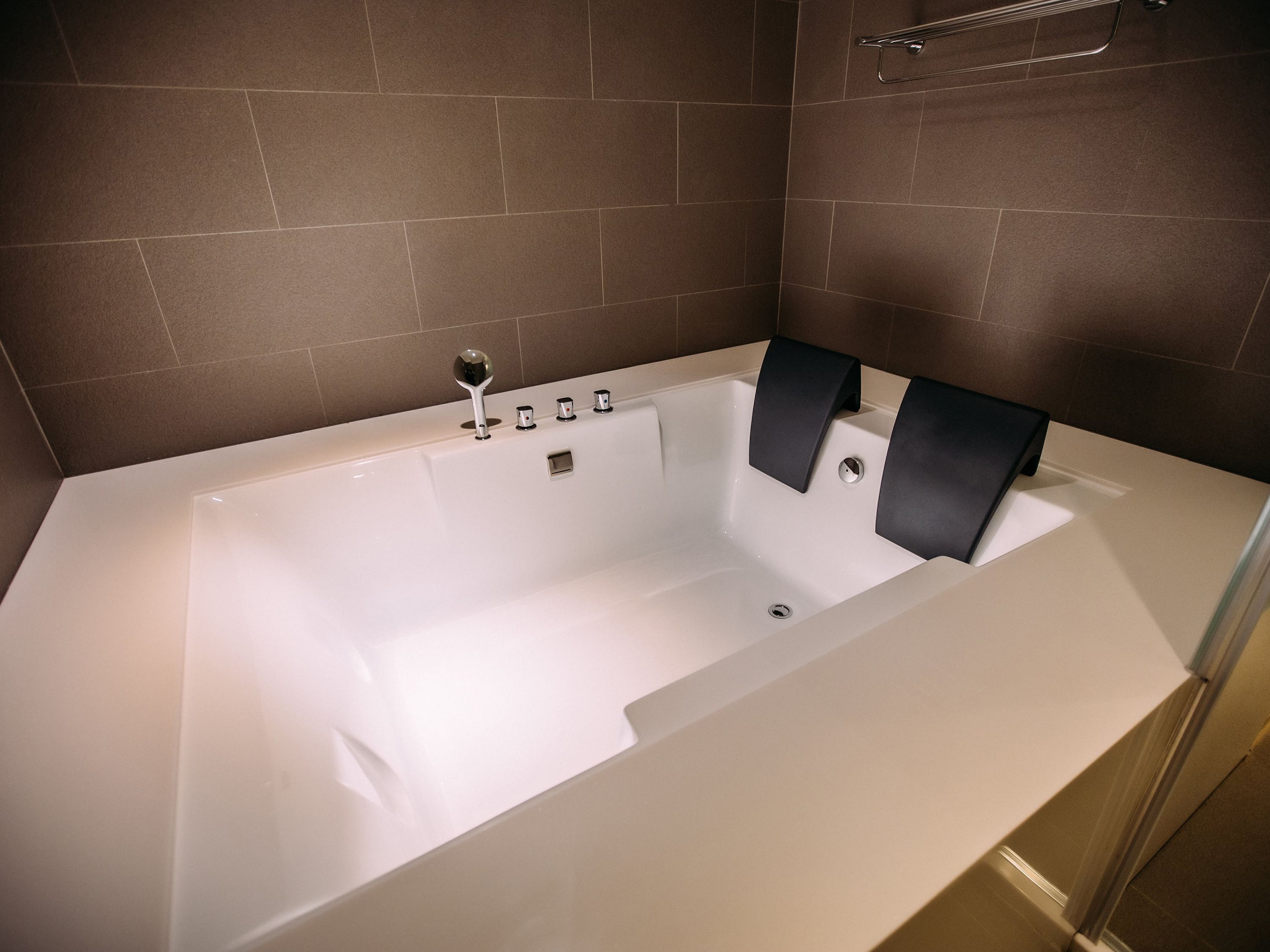 A modern bathroom with a white bathtub, a handheld showerhead, and a towel rack.