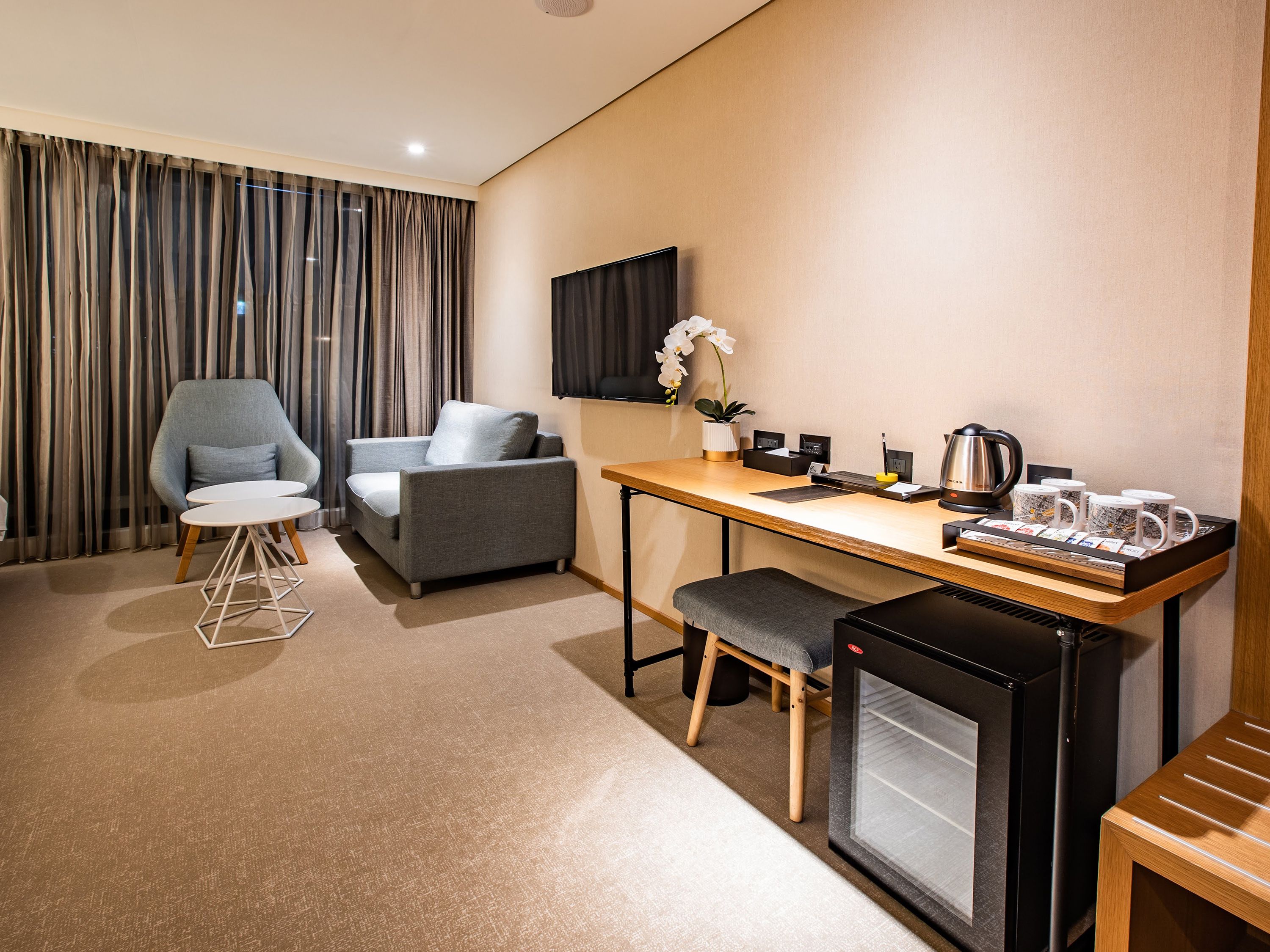 Une chambre d’hôtel équipée d’un canapé, d’un fauteuil, d’une petite table, d’un coin café et d’un mini-réfrigérateur.