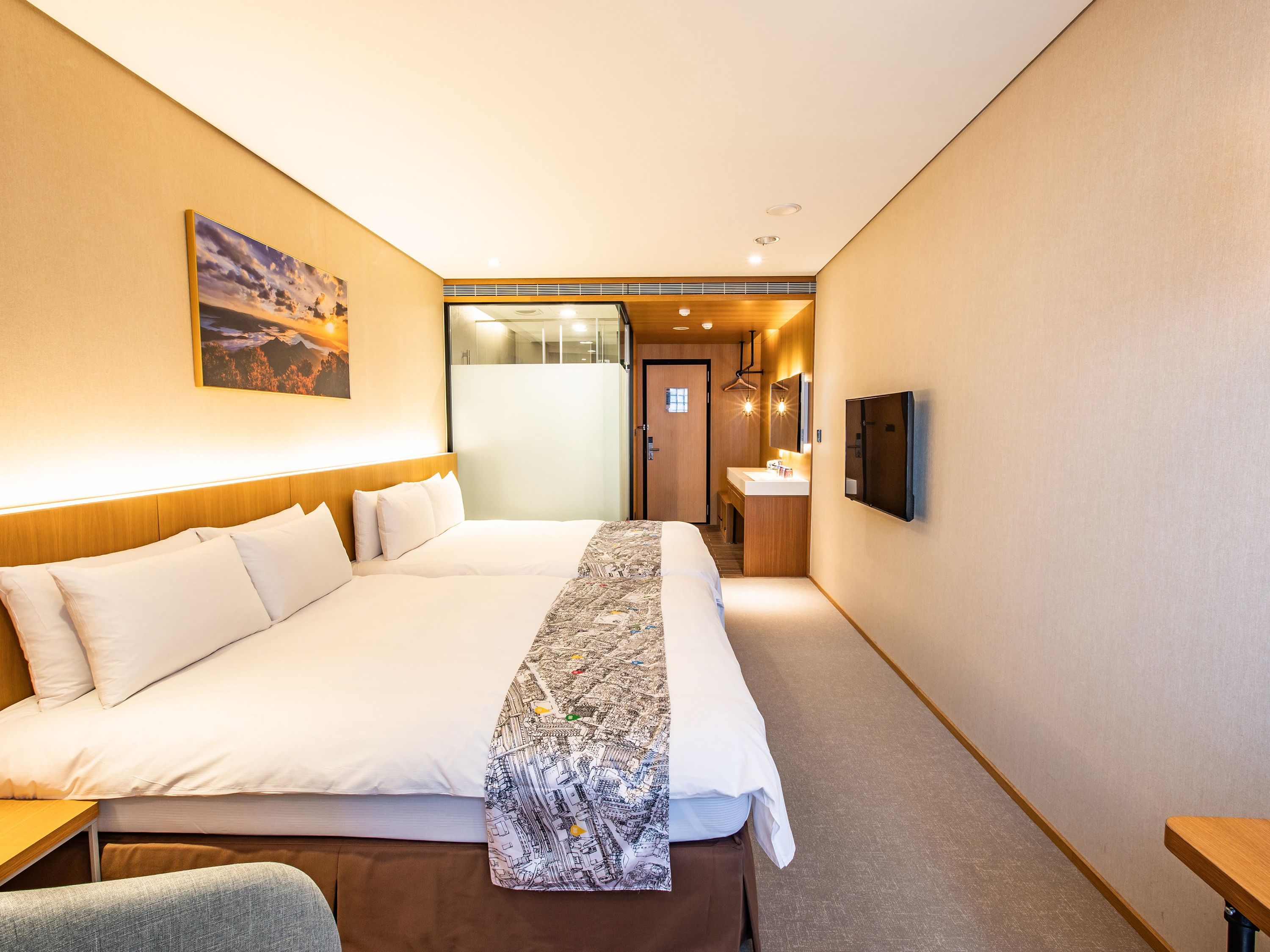 A hotel room with a large bed, a bedside table, a desk, a mirror, and a wall-mounted TV.