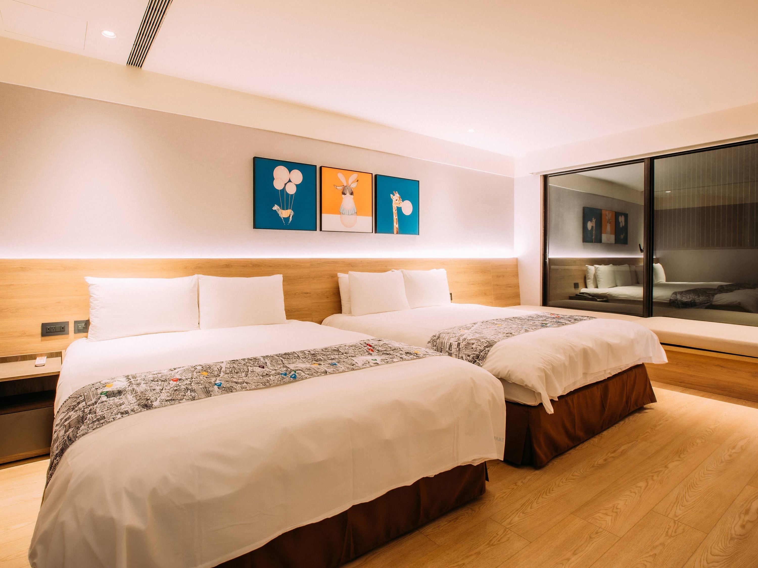 Ein Hotelzimmer mit zwei Betten, einem großen Fenster und Kunstwerken an der Wand.