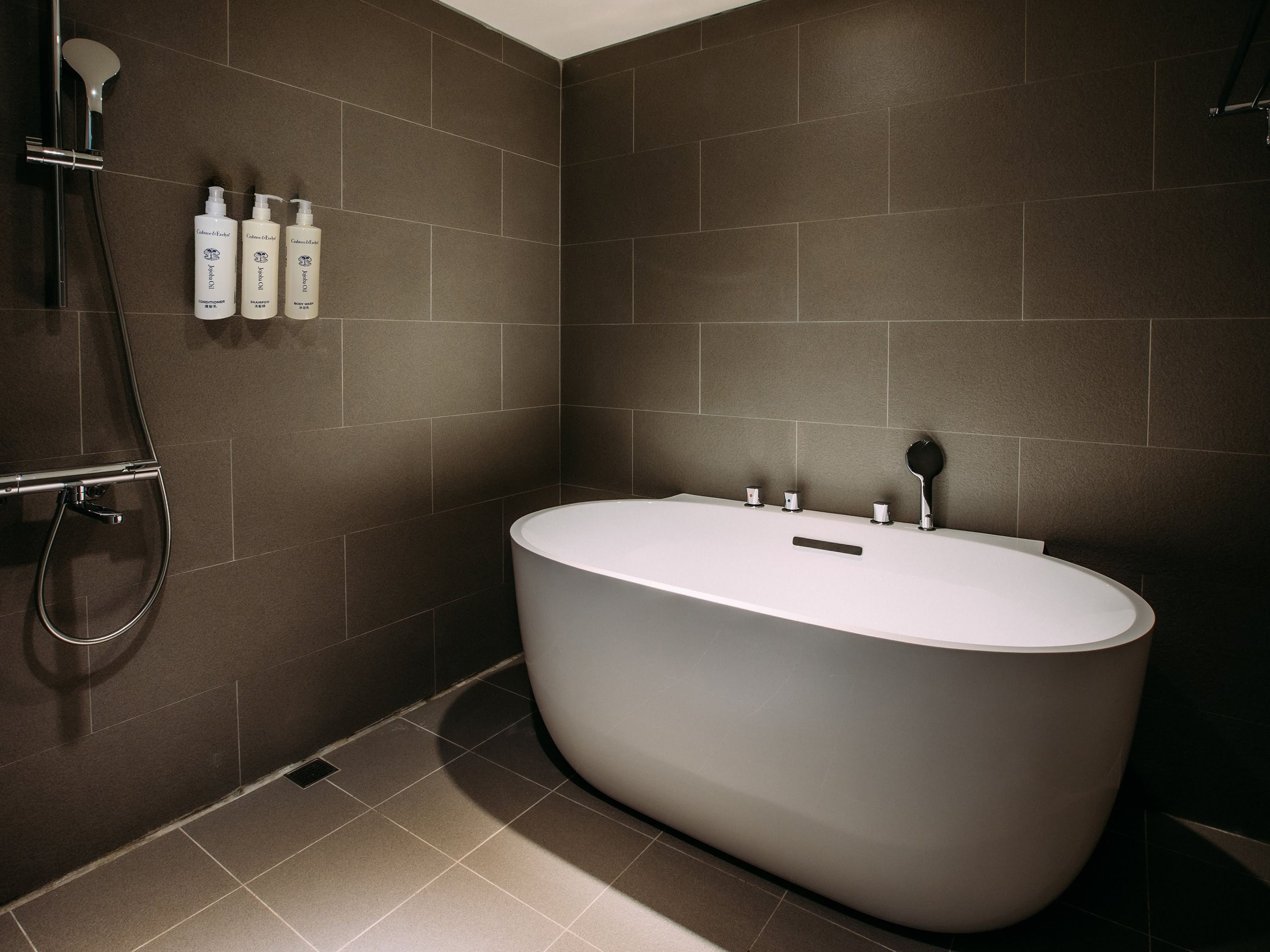 Ein modernes Badezimmer mit einer freistehenden Badewanne, einer Handbrause und drei Flüssigseifenflaschen an der Wand.