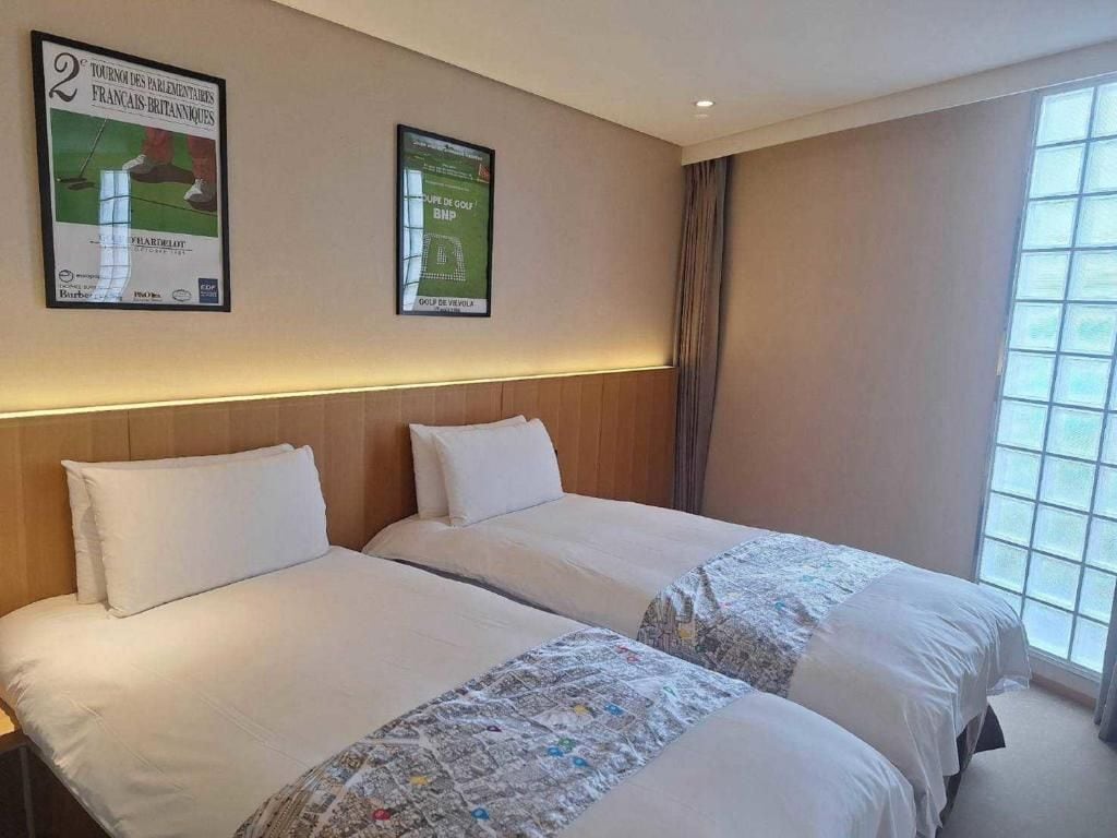 A hotel room with two beds, a large window, and two posters on the wall.