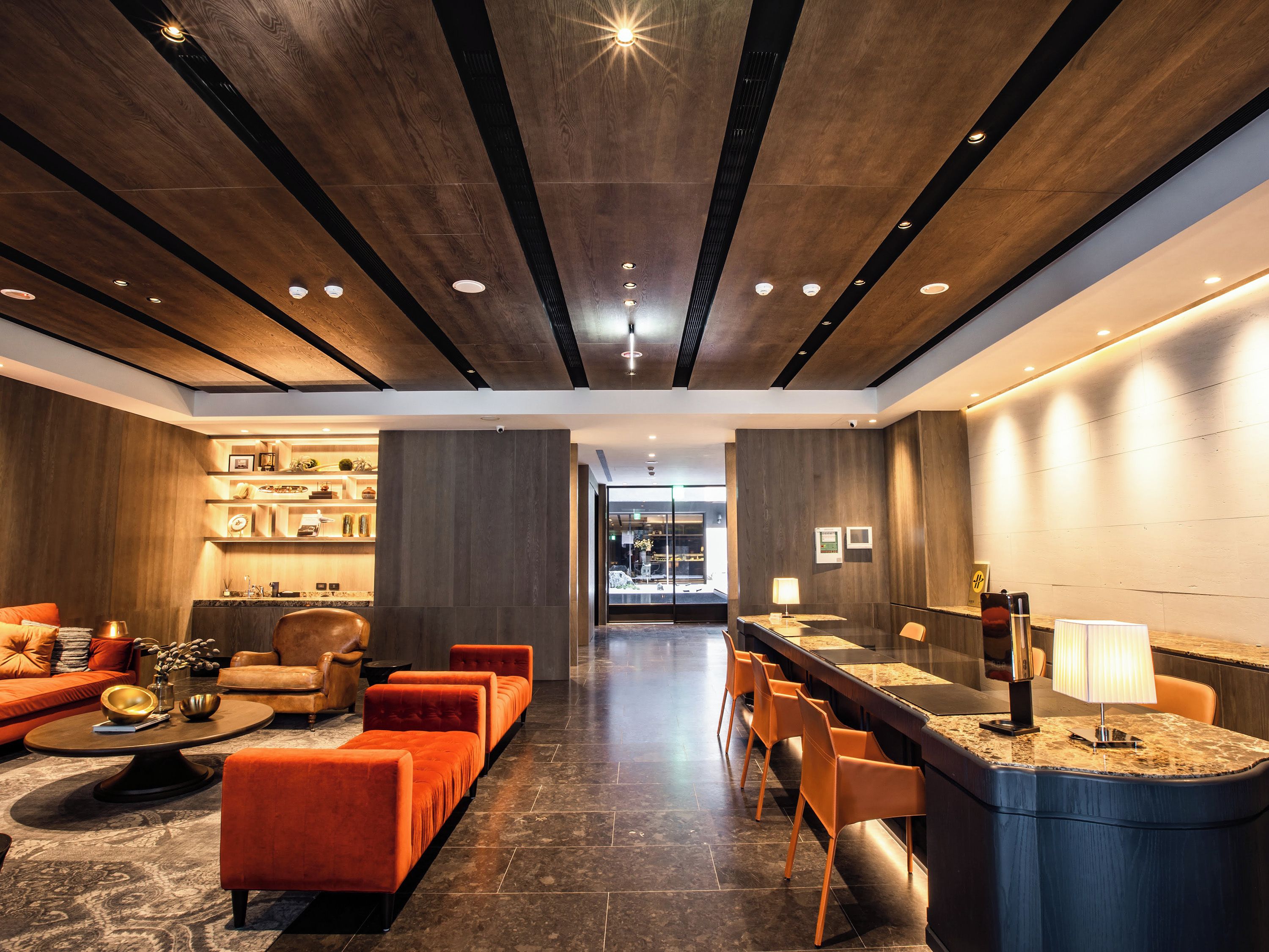A modern hotel lobby with a reception desk, seating area, and a view into the dining area.