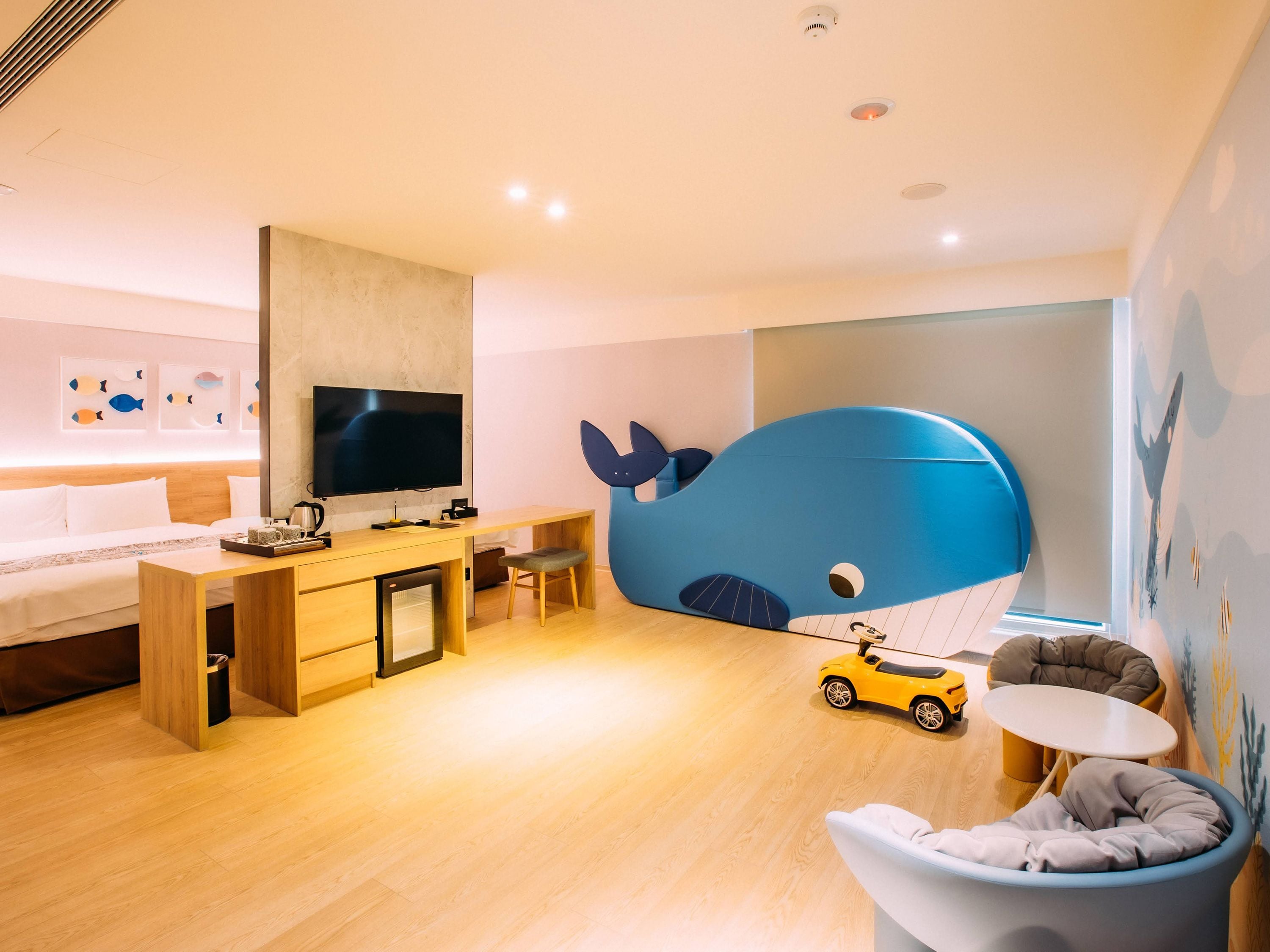 Quarto moderno com cama, escrivaninha, televisão e uma grande cabeceira com tema de baleia.