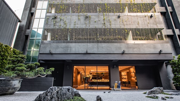 A modern building with a glass entrance, a gravel courtyard, and a bonsai tree.