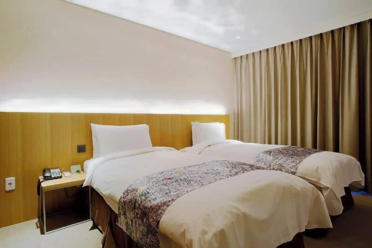 Una habitación de hotel con dos camas, un cabecero de madera, una mesita de noche con un teléfono y una cortina.