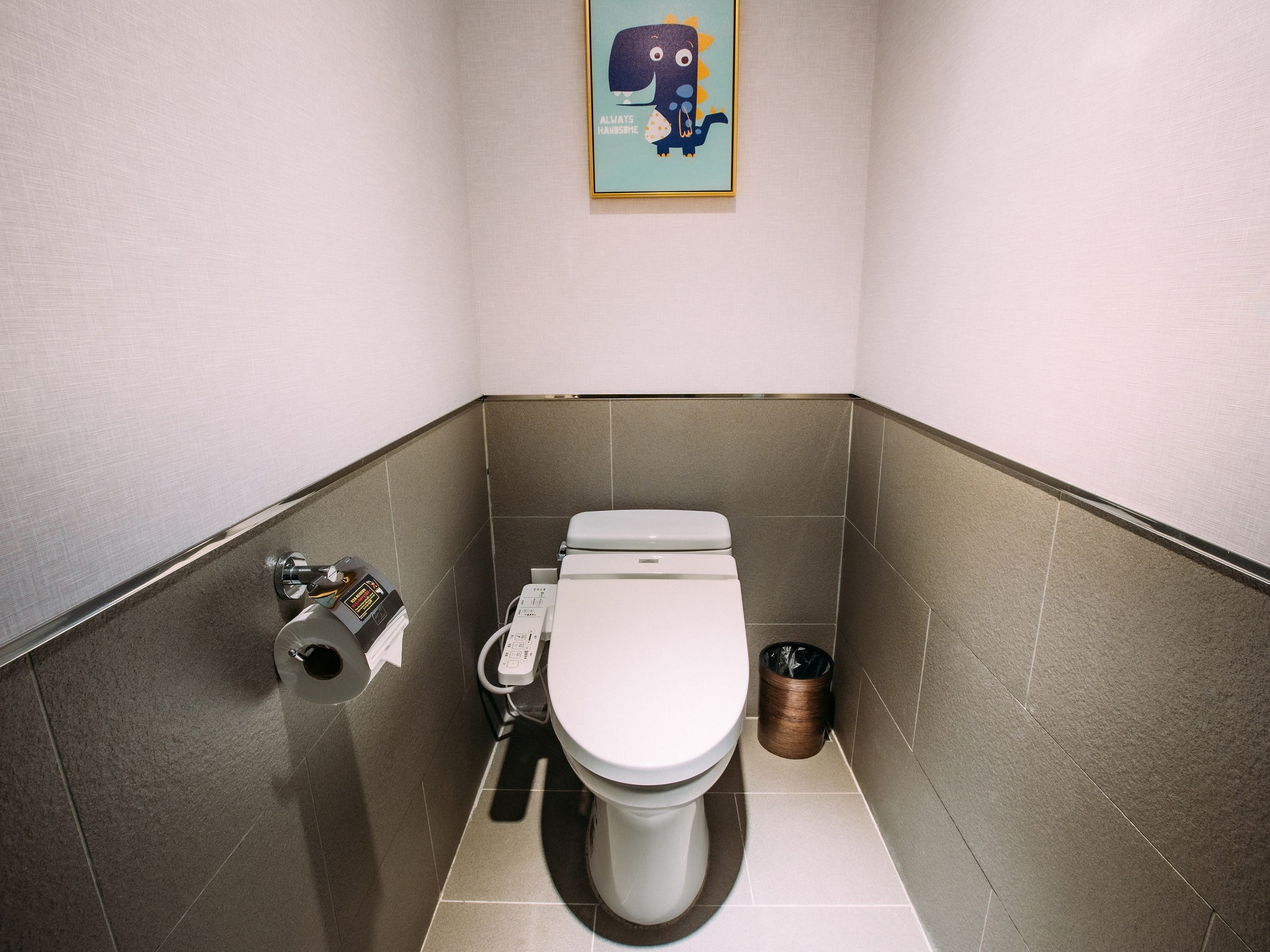 A small, modern bathroom with a toilet, a hand dryer, and a trash can.