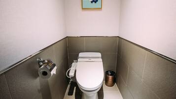 A small, modern bathroom with a toilet, a hand dryer, and a trash can.