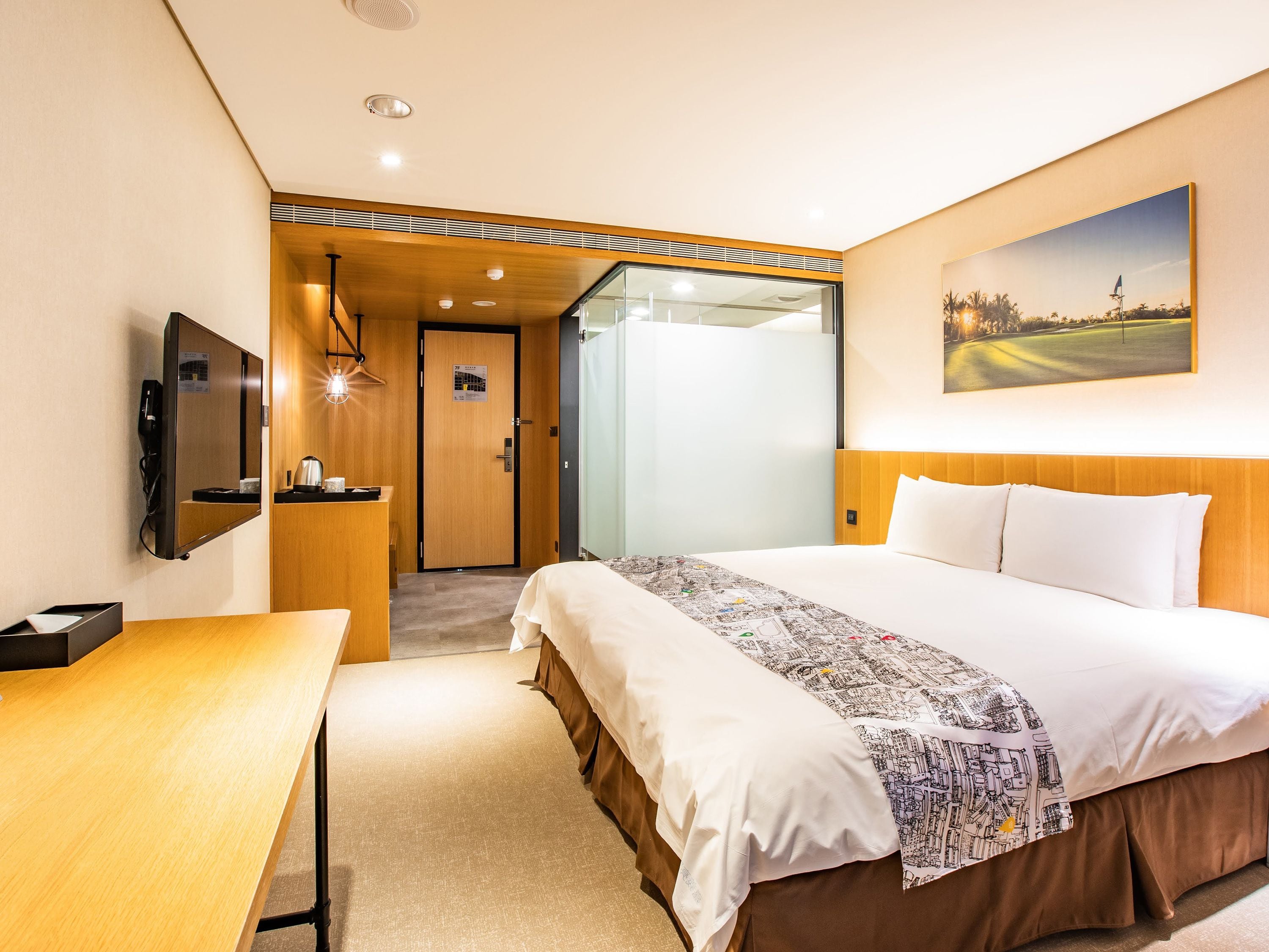 A hotel room with a bed, a desk, a TV, and a painting on the wall.
