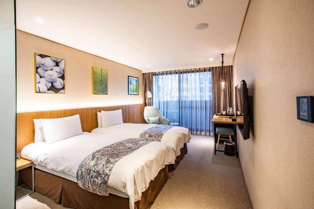 A hotel room with two beds, a desk, a chair, and a TV.