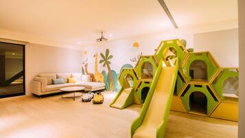 A modern living room with a sofa, coffee table, and children's play area including slides and geometric play structures.