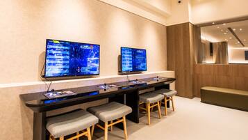 A modern reception area with a long counter, two monitors displaying content, and a seating area with stools.