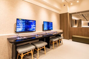 A modern reception area with a long counter, two monitors displaying content, and a seating area with stools.