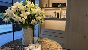A marble table with a vase of white lilies, a book, and a bottle of perfume.