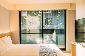 Ein Hotelzimmer mit einem großen Bett, einem Fernseher und einem Fenster mit Blick auf ein Gebäude und Bäume.