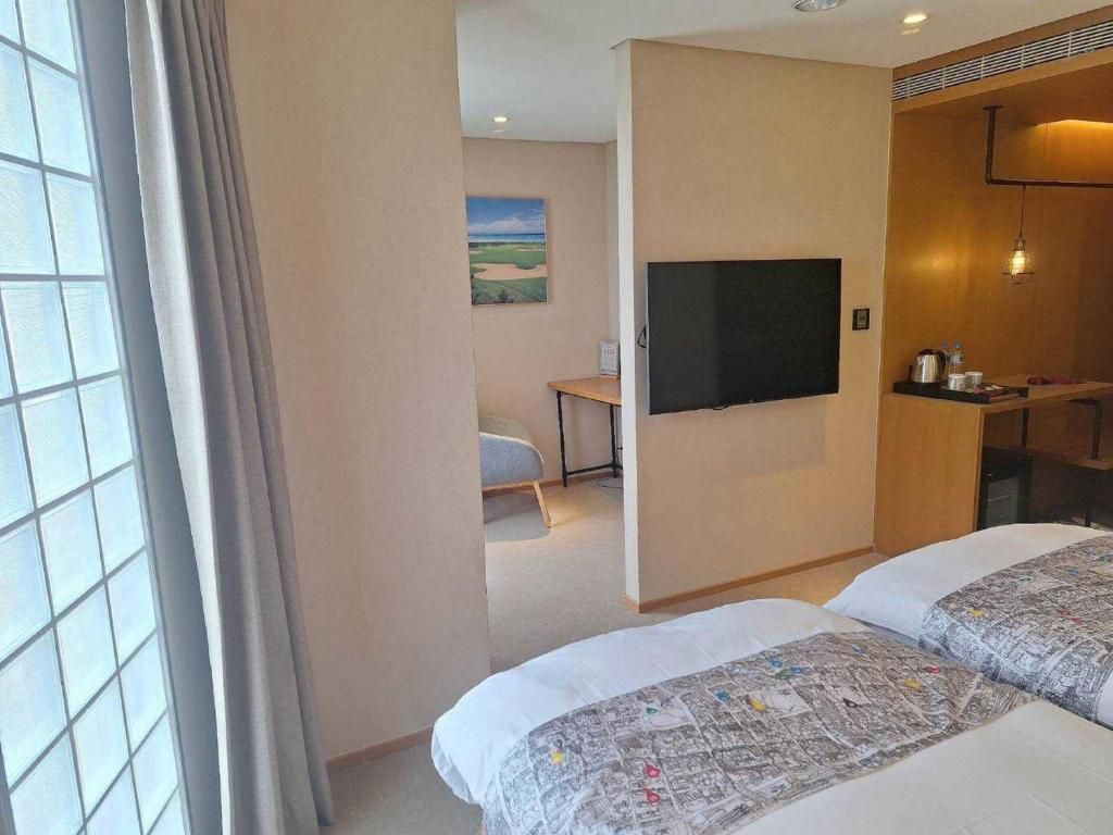 A hotel room with two beds, a television mounted on the wall, a desk with a chair, and a painting on the wall.