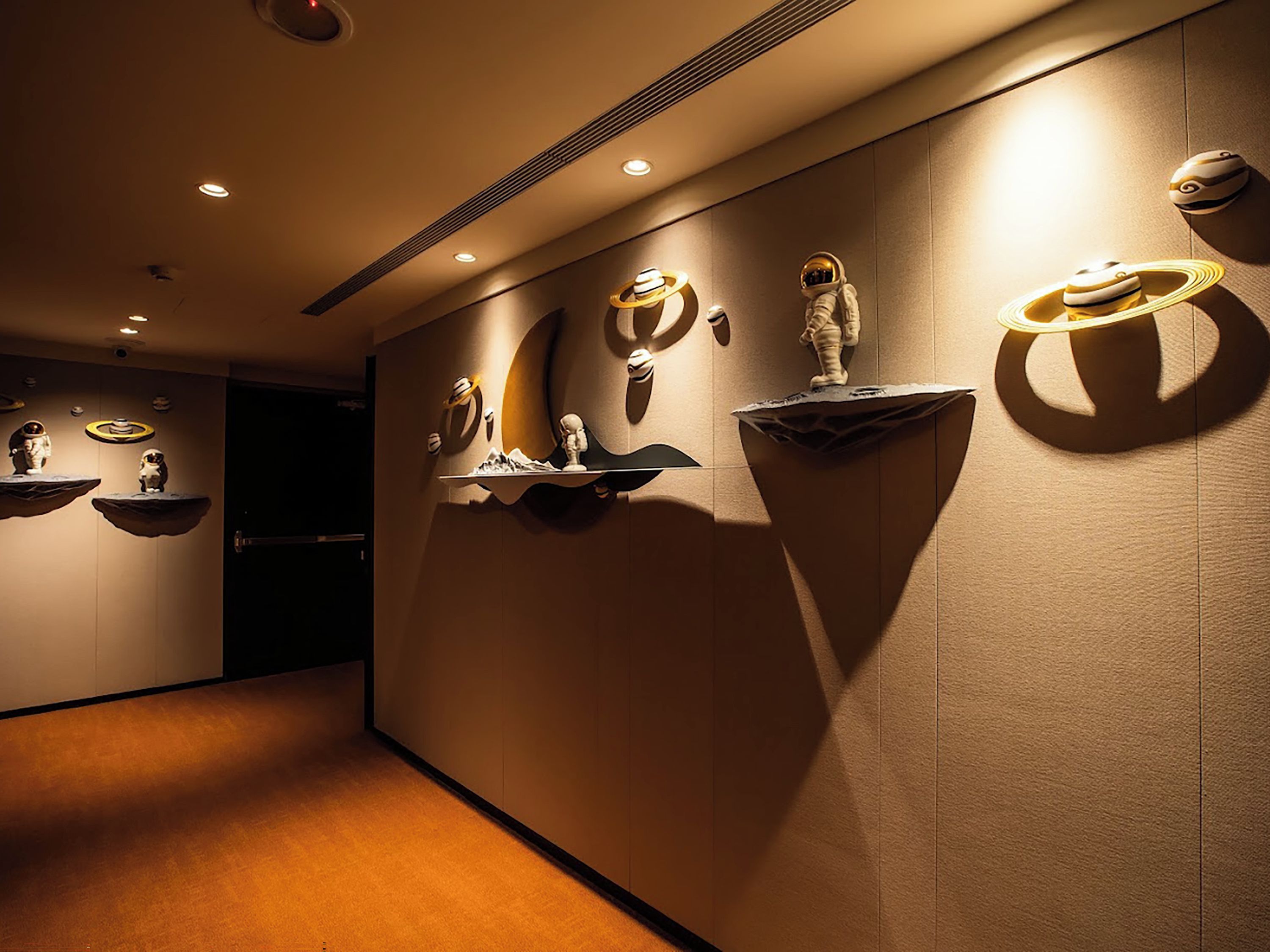 A hallway with wall-mounted sculptures and recessed lighting.