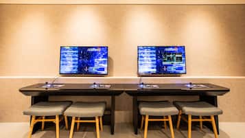 Una sala de conferencias con dos monitores grandes mostrando el mismo contenido, una mesa larga y cuatro taburetes grises acolchados.