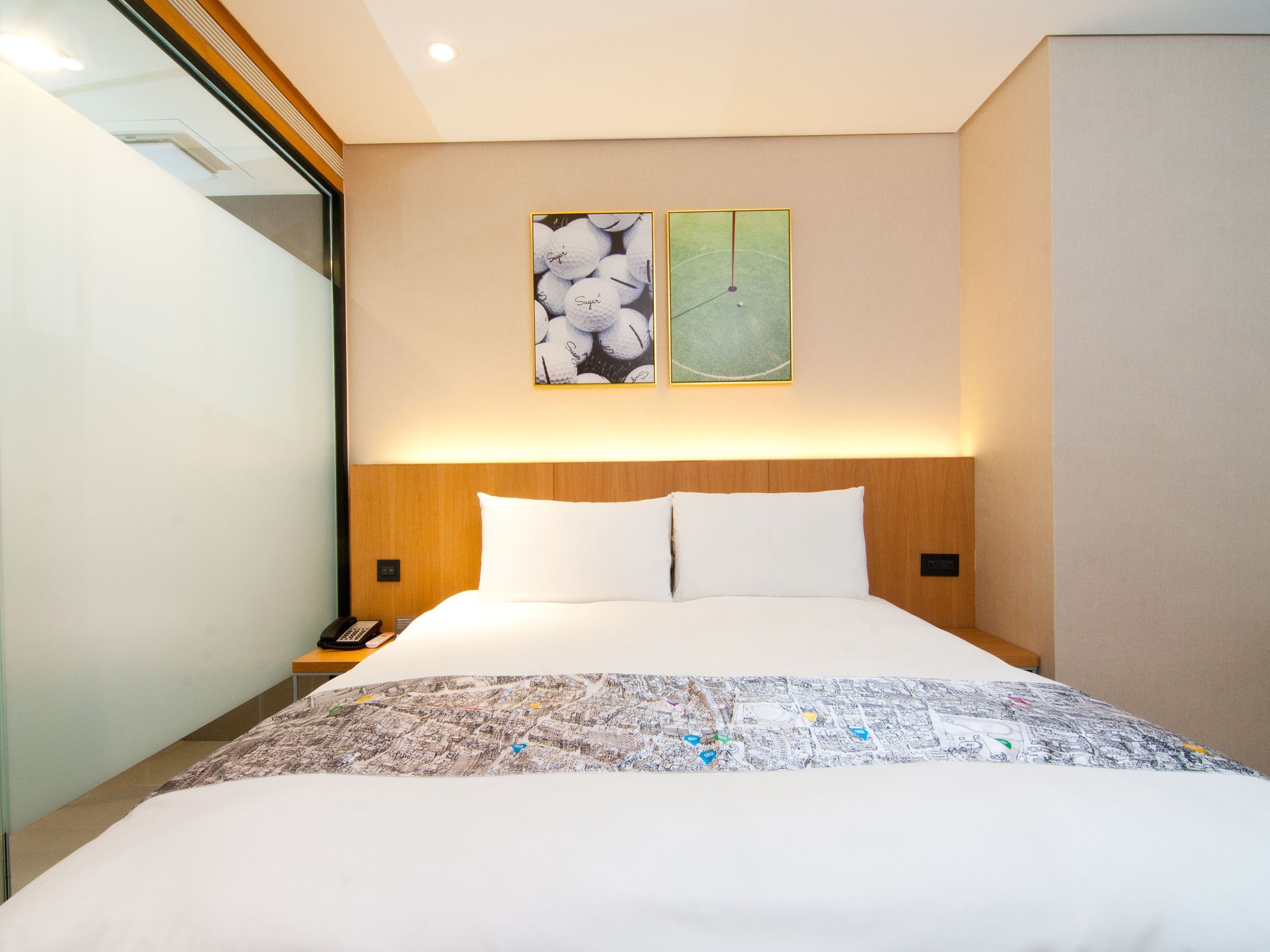 A hotel room with a large bed, a nightstand with a phone, and two wall-mounted paintings.