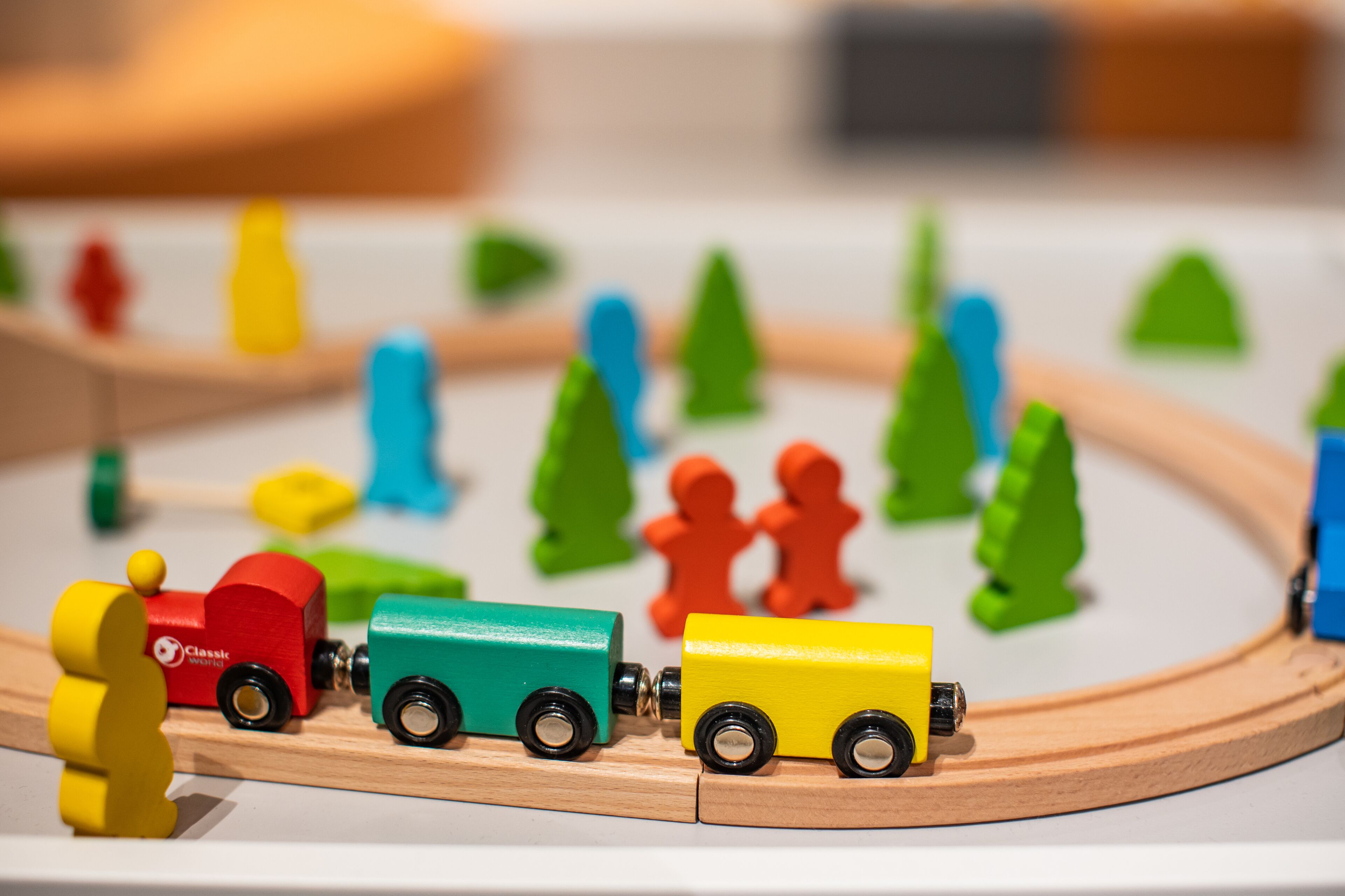 A wooden toy train set with a red locomotive, a green car, and a yellow car on a track.