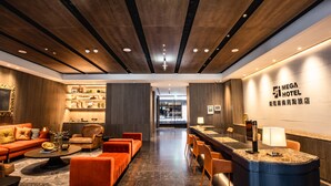 A modern hotel lobby with a reception desk, seating area, and a view into the restaurant.