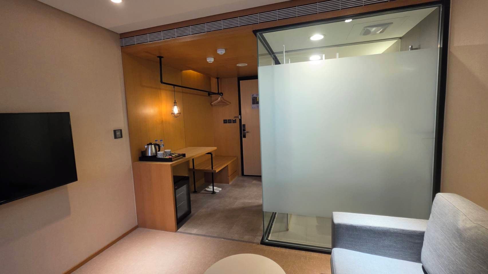 Habitación de hotel compacta con televisor de pantalla plana, una kitchenette pequeña, una zona de estar y un separador de vidrio.