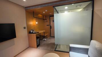 Habitación de hotel compacta con televisor de pantalla plana, una kitchenette pequeña, una zona de estar y un separador de vidrio.