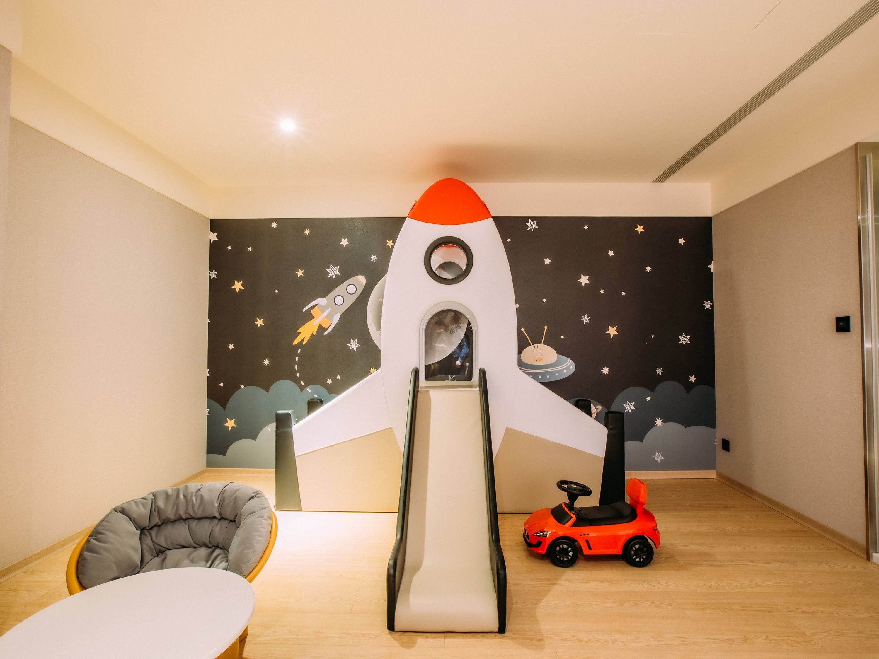 Une pièce avec un toboggan en forme de fusée, une petite voiture jouet et une chaise.