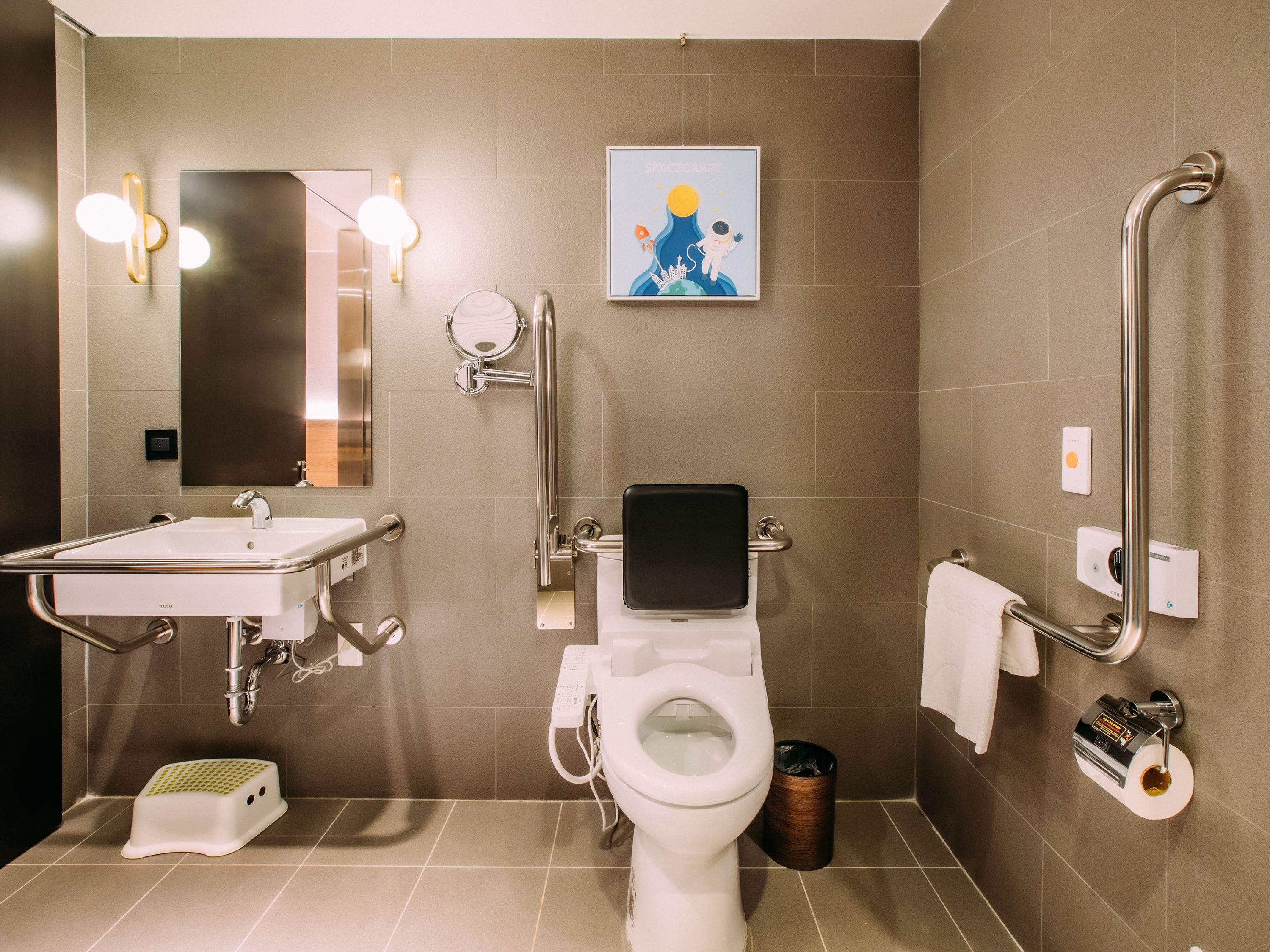 A modern bathroom with a toilet, bidet, and sink, equipped with accessibility features like grab bars and a step stool.