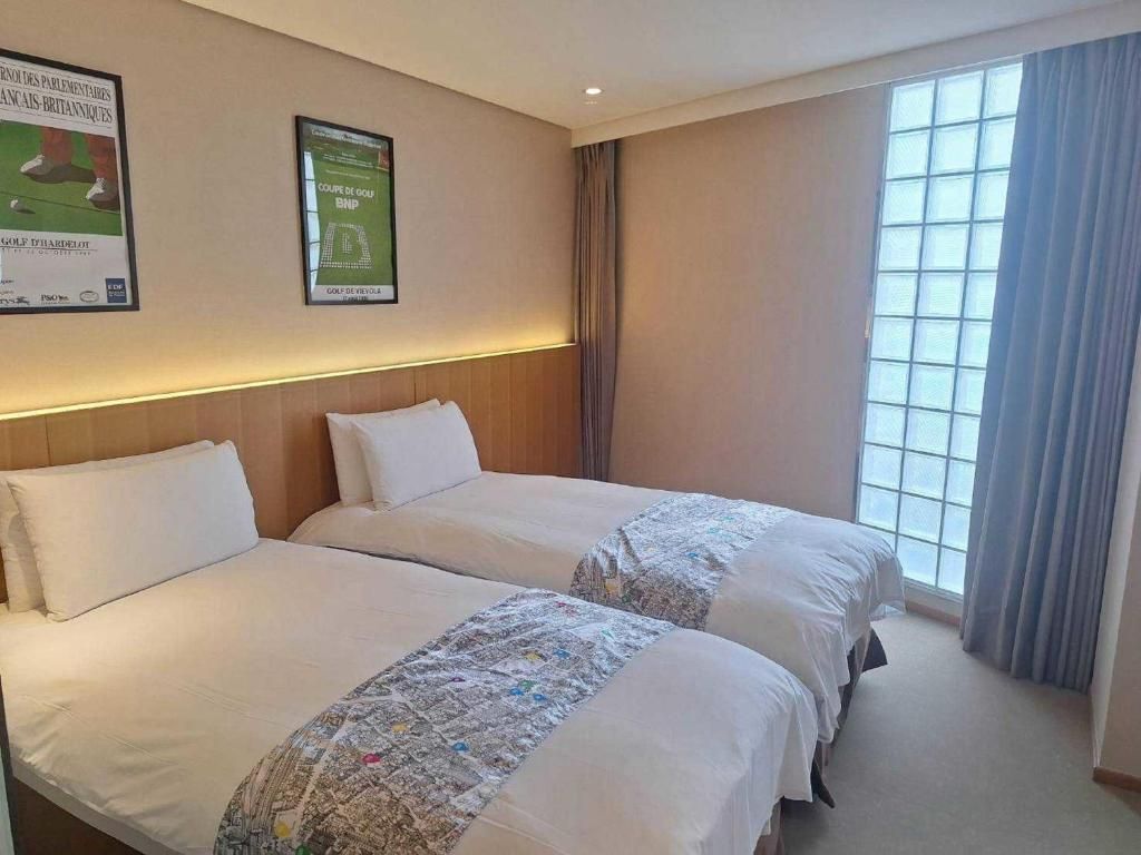 A hotel room with two beds, a large window with curtains, and wall decorations.