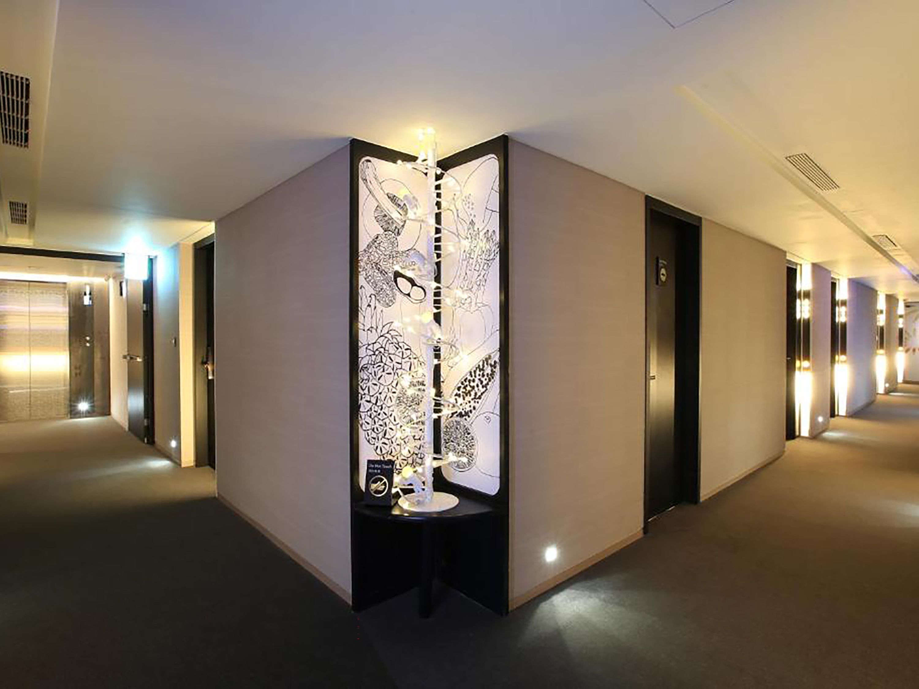 A hotel corridor with a central decorative partition featuring abstract patterns, a door on the right, and a staircase on the left.