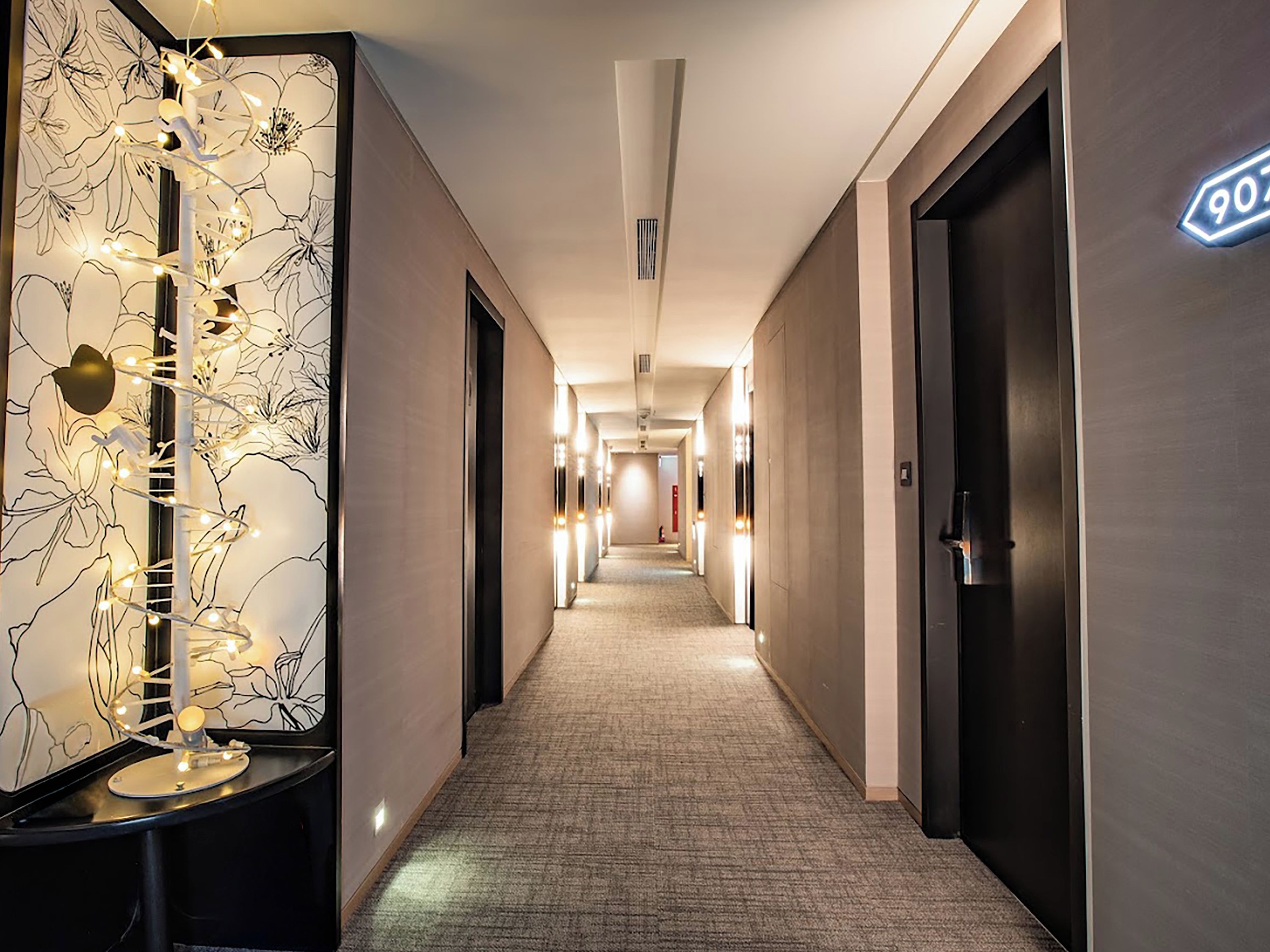 A hotel corridor with a patterned wall, a light fixture, and a door with a number sign.