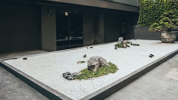 A courtyard with a gravel ground, a rock formation, and a potted plant.