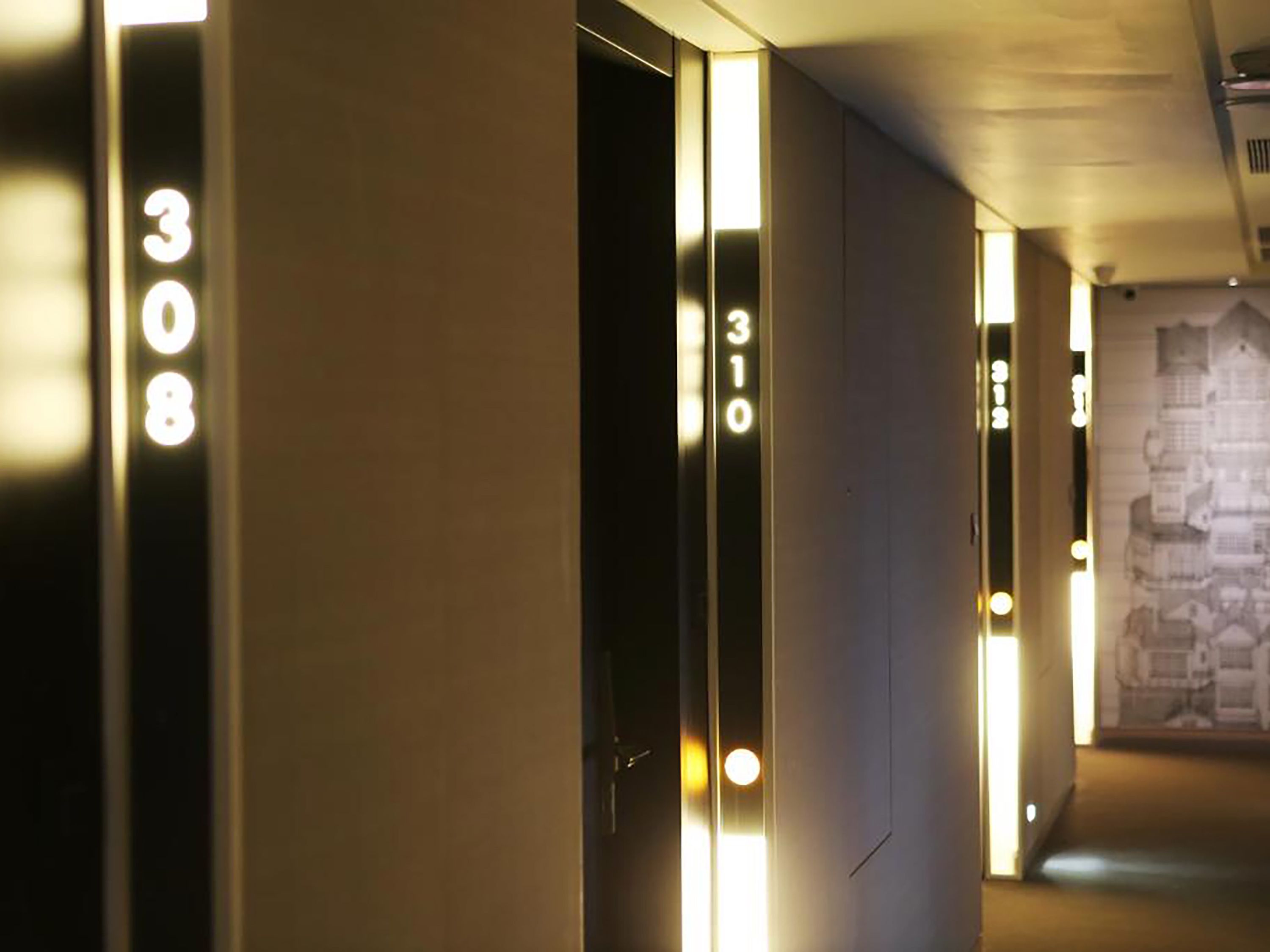 A hotel corridor with illuminated room numbers, a modern design, and a patterned wall in the background.