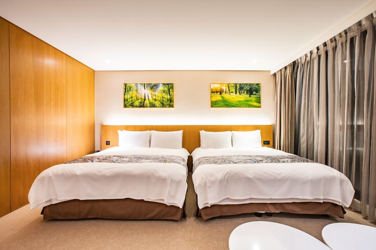 Habitación de hotel con dos camas, una pared de madera y dos cuadros enmarcados.